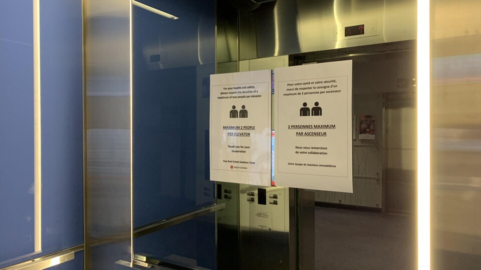 L'intérieur d'un ascenseur, avec une affiche qui indique qu'un maximum de deux personnes peuvent occuper l'espace à la fois.
