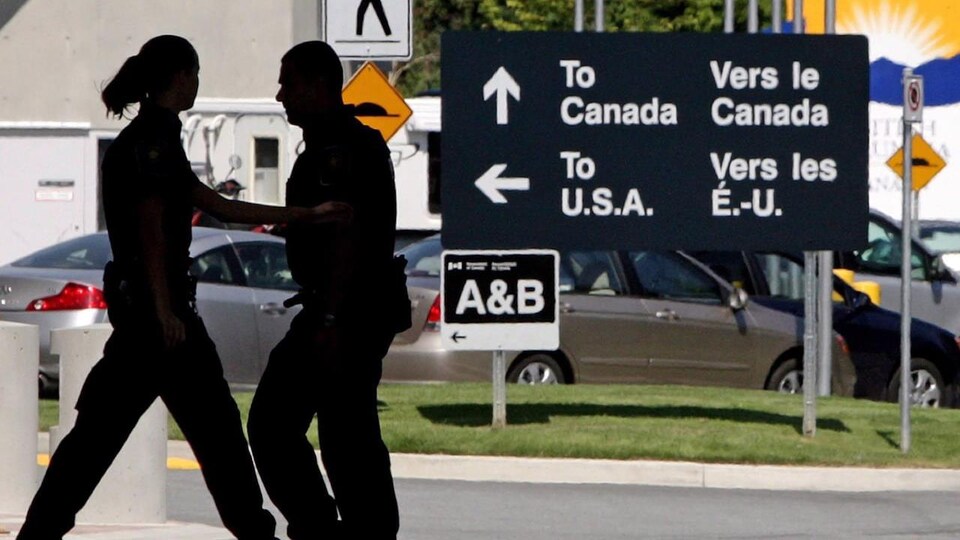 Two CBSA officers in front of the backlit vehicles.