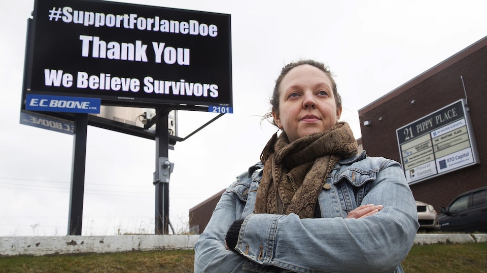 Ashley MacDonald pose devant un panneau sur lequel est écrit : #supportforjanedoe thank you we believe survivors.