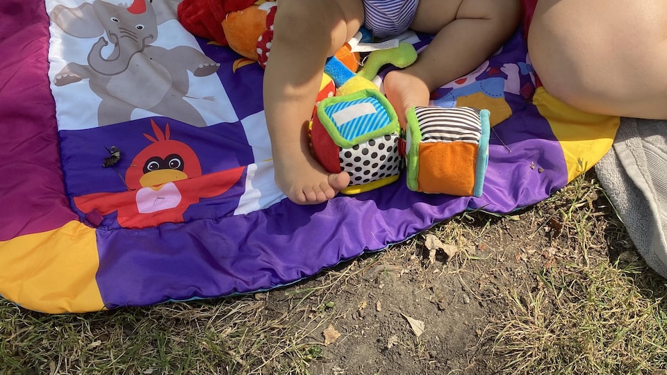 Un enfant sur une couverture entouré de ses jouets.