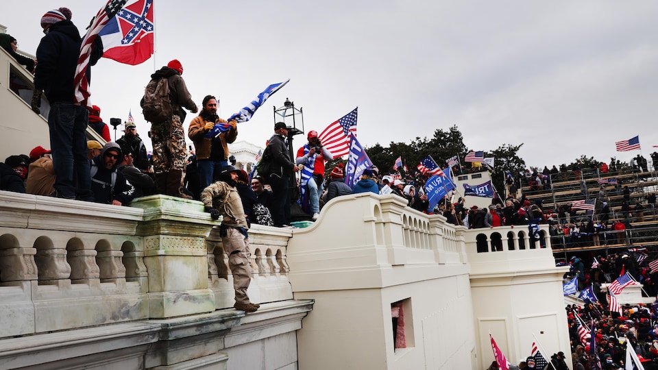 Des partisans de Donald Trump à l'extérieur du Capitole, qu'ils ont pris d'assaut; certains portent des drapeaux américains ou pro-Trump.