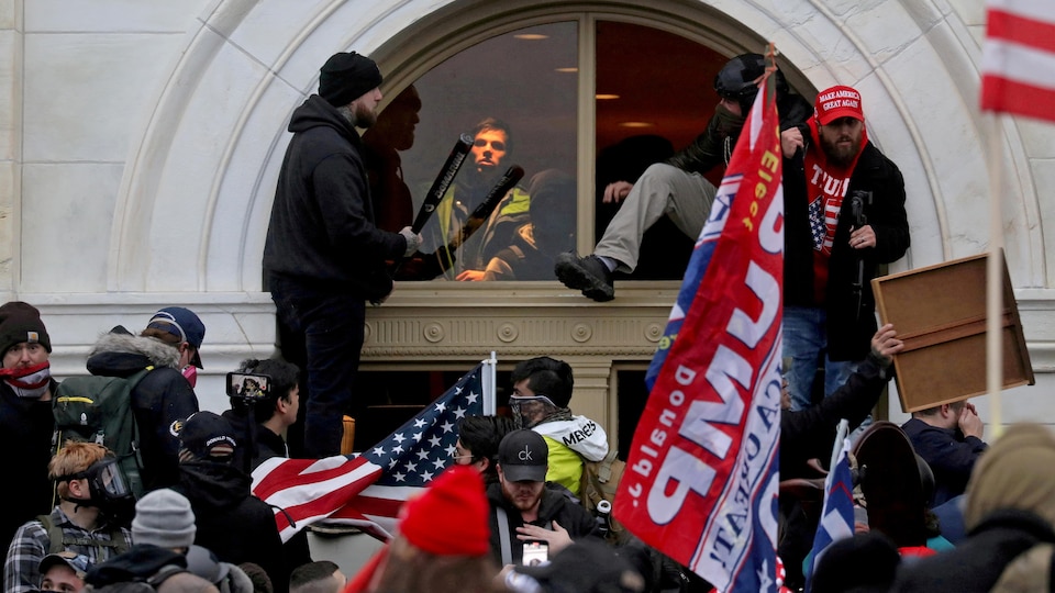 Des partisans de Donald Trump, dont certains portent des drapeaux américains ou pro-Trump, grimpent dans le Capitole à travers une fenêtre qu'ils ont brisée.