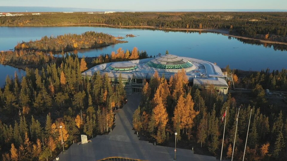 Vue aérienne de l'Assemblée législative des Territoires du Nord-Ouest située dans un secteur boisé près d'un lac.