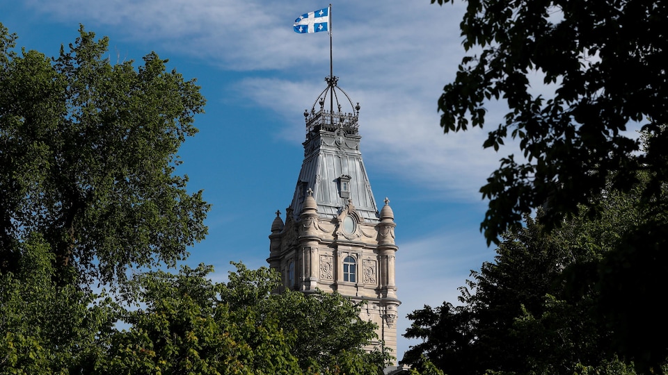 La tour coiffée du drapeau du Québec est vue à travers des arbres.