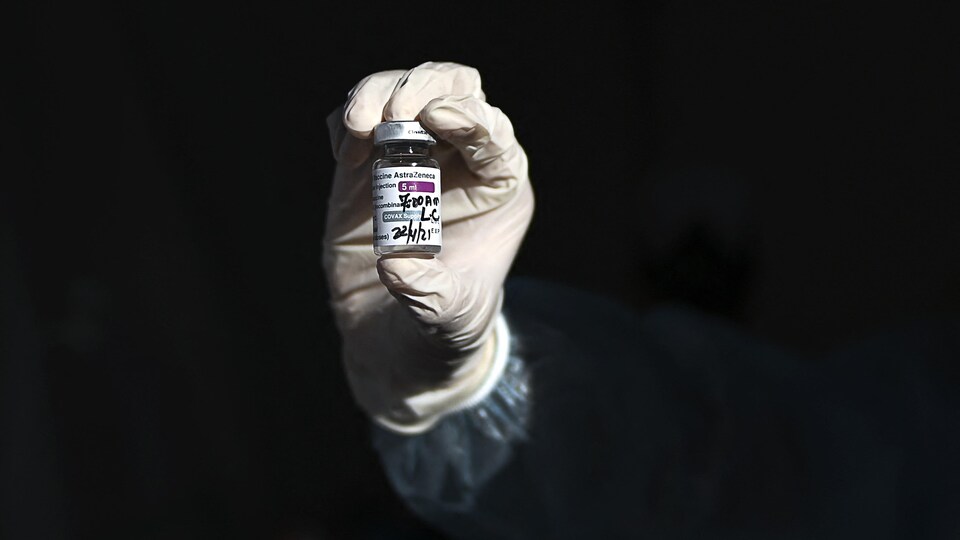 Une main gantée tient une fiole du précieux vaccin.
