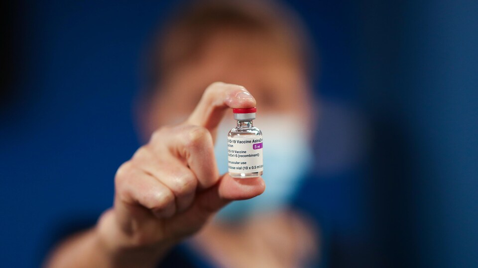 Une fiole du vaccin d'AstraZeneca entre le pouce et l'index d'une travailleuse de la santé qui la montre à la caméra.