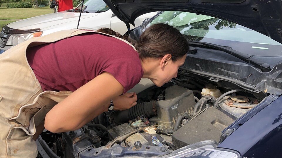 Une femme inspecte le moteur d’une voiture.