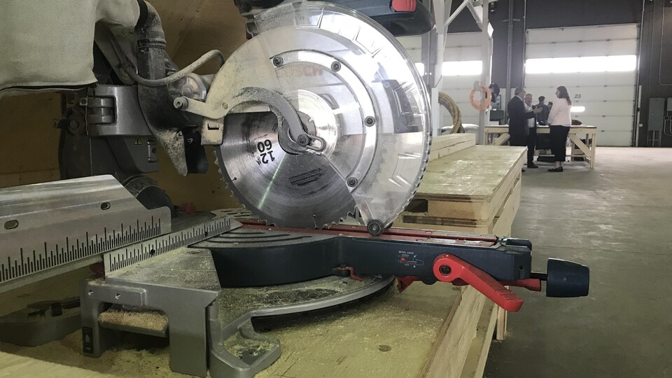 Une scie industrielle dans un hangar avec des gens qui discutent en arrière-plan.