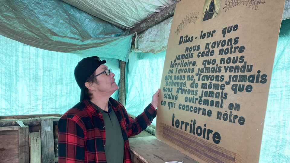 Alain Ottawa regarde un panneau sur lequel est écrit : « Dites-leur que nous n'avons jamais cédé notre territoire ». 