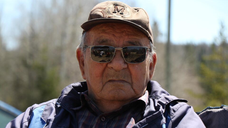 Un homme âgé de face portant une casquette et des lunettes de soleil.