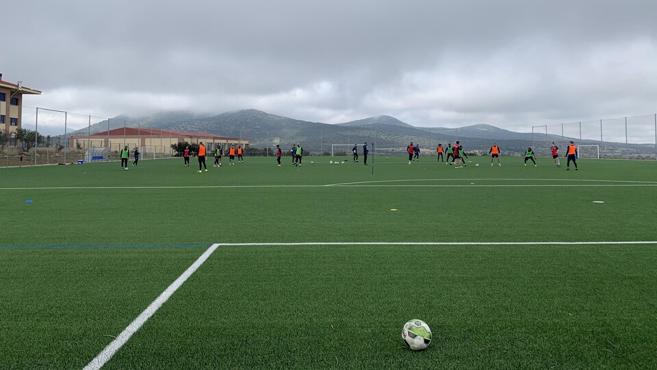 Un terrain de soccer avec un ballon à l'avant-plan et les joueurs derrière.