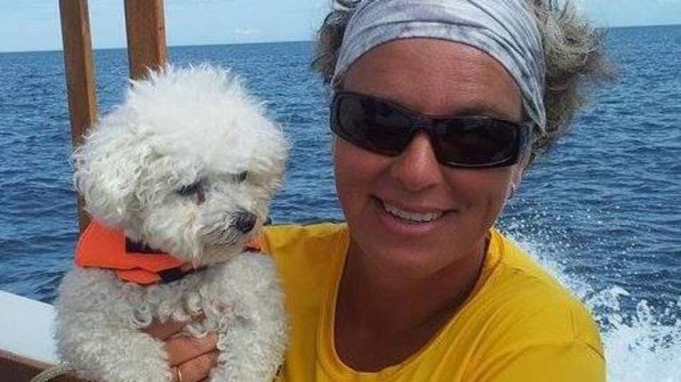 Anne Babin tient son petit bichon frisé dans ses bras sur un bateau.
