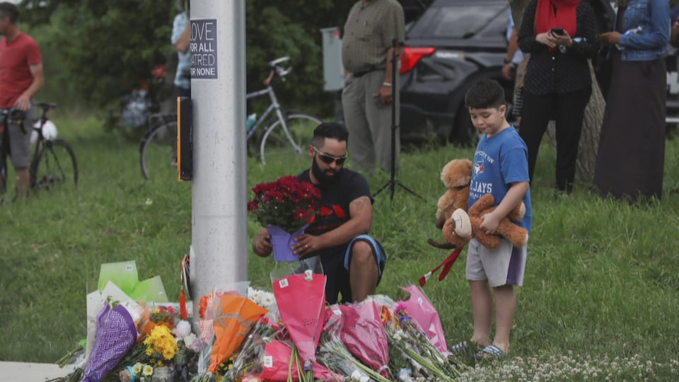 Un homme et un garçon déposent des fleurs et des peluches autour d'un feu de circulation.