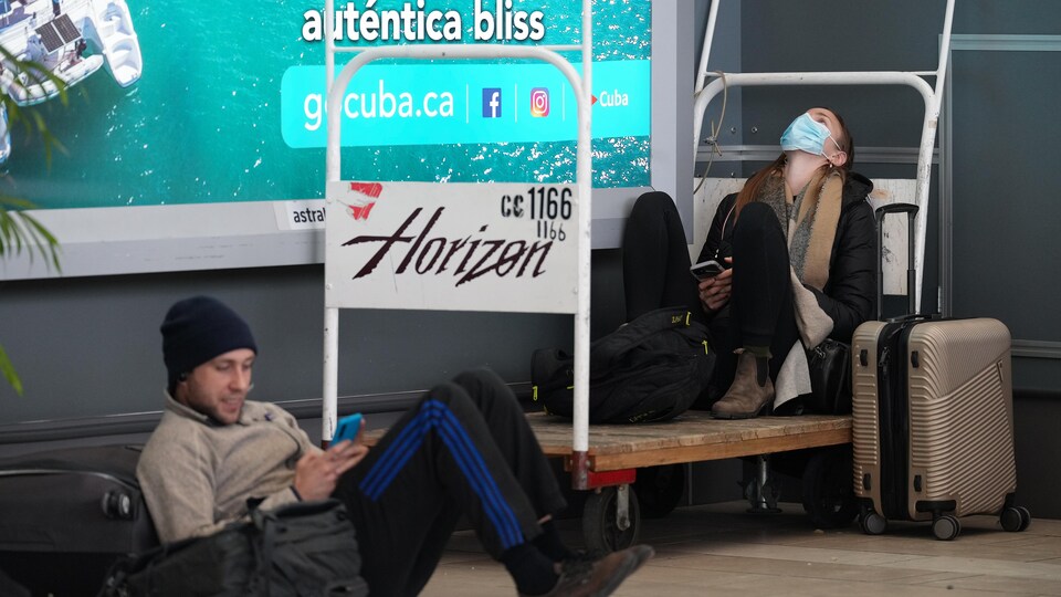 Des passagers assis par terre attendent avec leurs sacs et valises à l'aéroport.