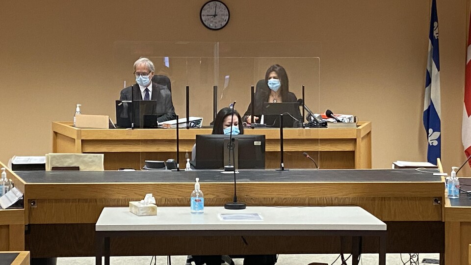 Trois personnes, dont la coroner Géhane Kamel, avec un masque, dans une salle du palais de justice de Shawinigan.
