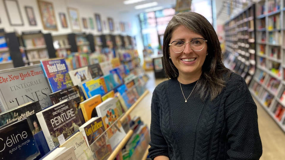 Une femme à lunettes et aux cheveux bruns debout dans une librairie, entourée de livres.