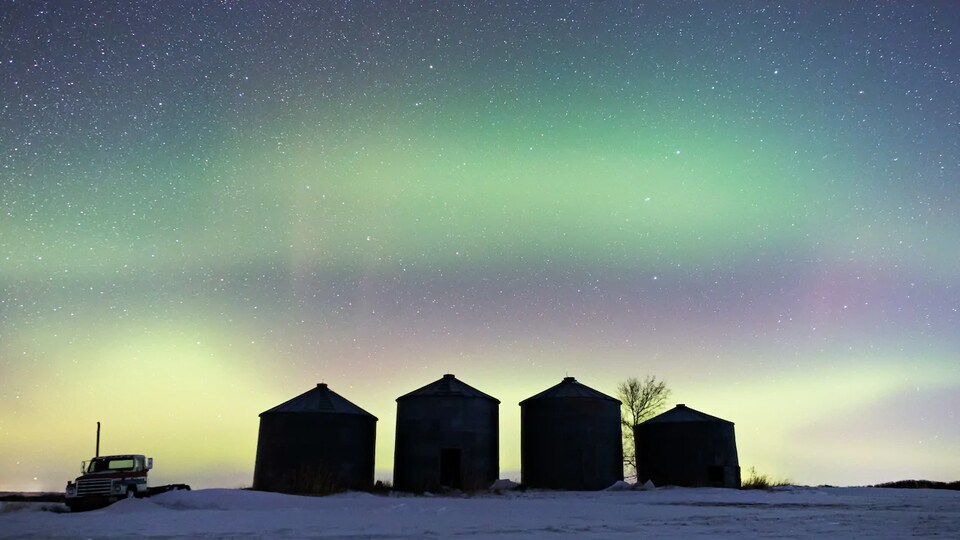 Quatre petits bâtiments sous un ciel qui montre des aurores boréales