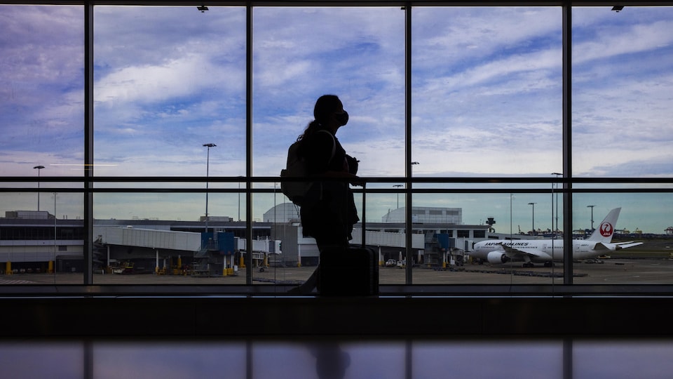Une personne masquée marche dans un terminal d'aéroport.