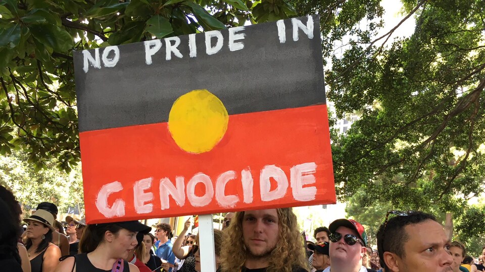 Un homme tient une affiche sur laquelle on peut lire : « Aucune gloire dans le génocide. »