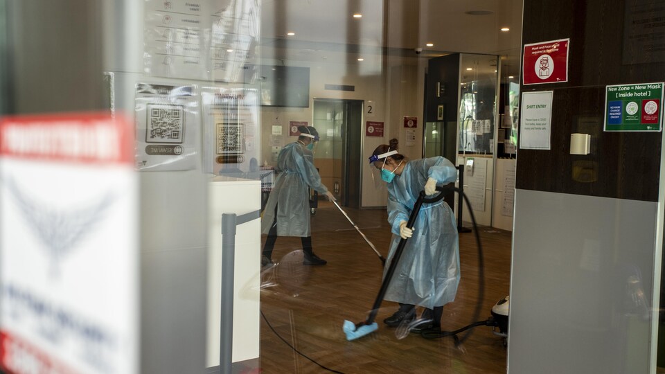 Deux femmes protégées de pied en cap nettoient un plancher.
