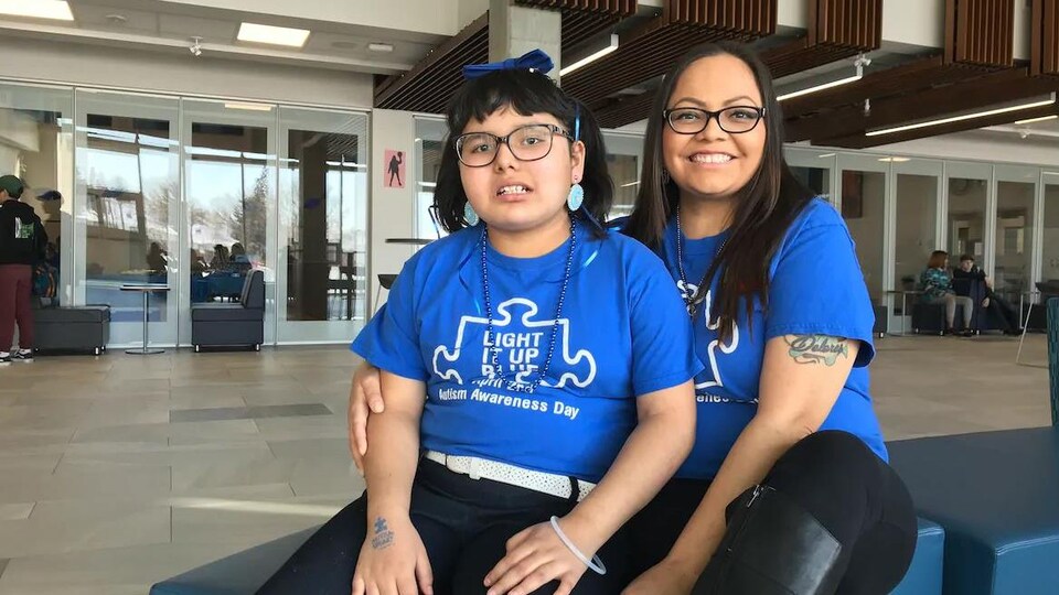 La mère et sa fille portent un chandail bleu, elles sont assises sur des poufs bleus au centre d'une grande salle.
