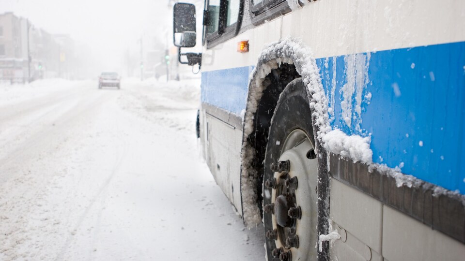 Un autobus circule sur une route enneigée. La visibilité est réduite par la brume et les précipitations de neige.