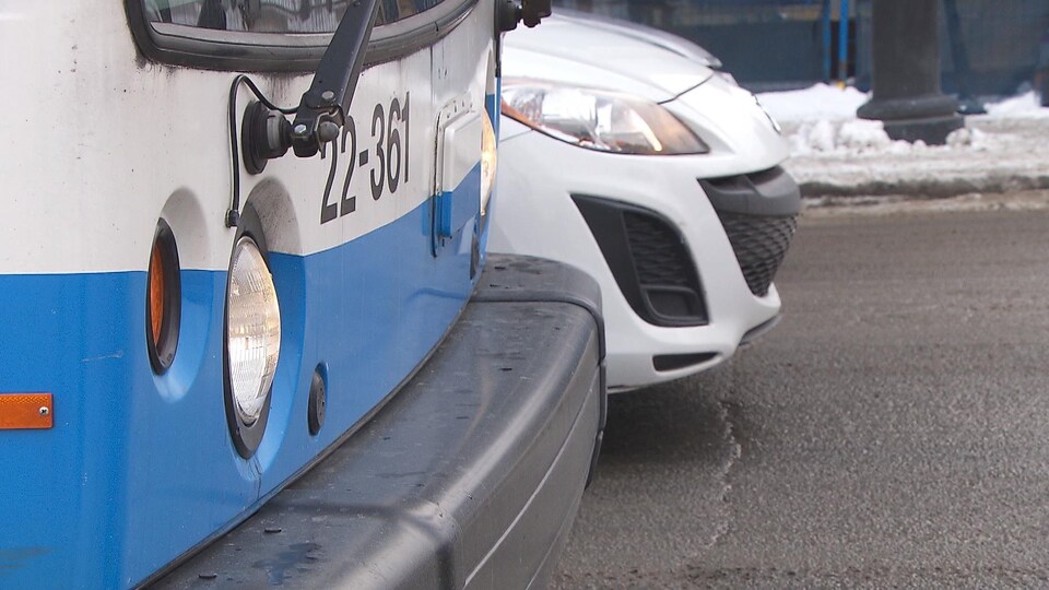 Un autobus de la STM à côté d'une voiture blanche à l'arrêt.