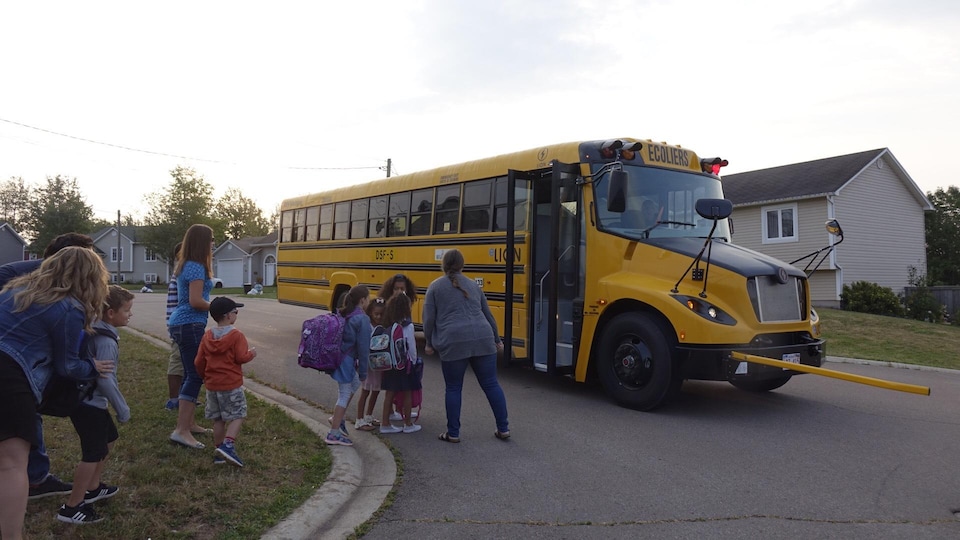 Des enfants qui embarquent dans l'autobus scolaire électrique. 
