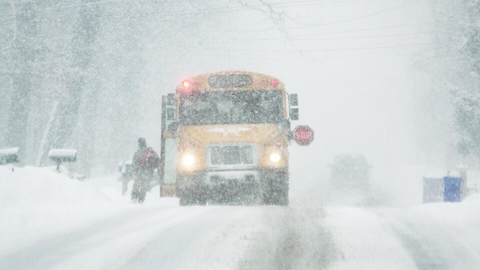 Un élève monte à bord d'un autobus scolaire pendant qu'il neige fortement.
