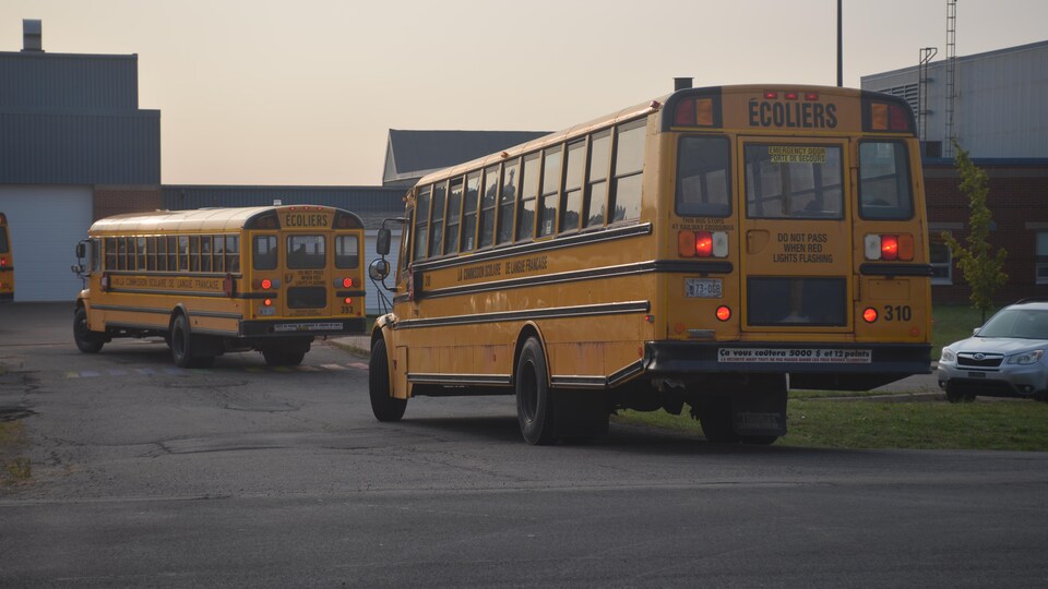 Deux autobus scolaires rentrent dans le stationnement de l'école François Buote. Les enfants sont à l'intérieur.