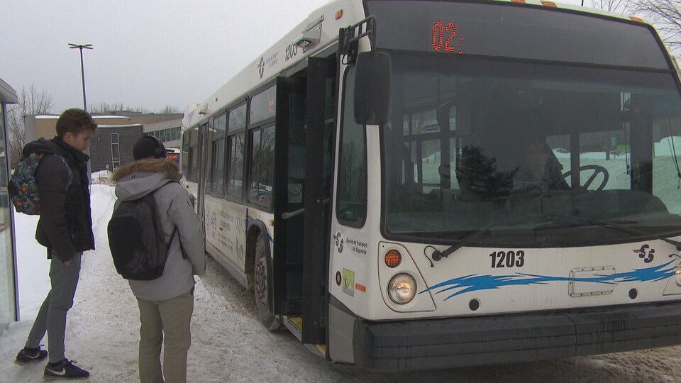 Un autobus de la STS avec deux étudiants qui attendent pour embarquer à l'intérieur.