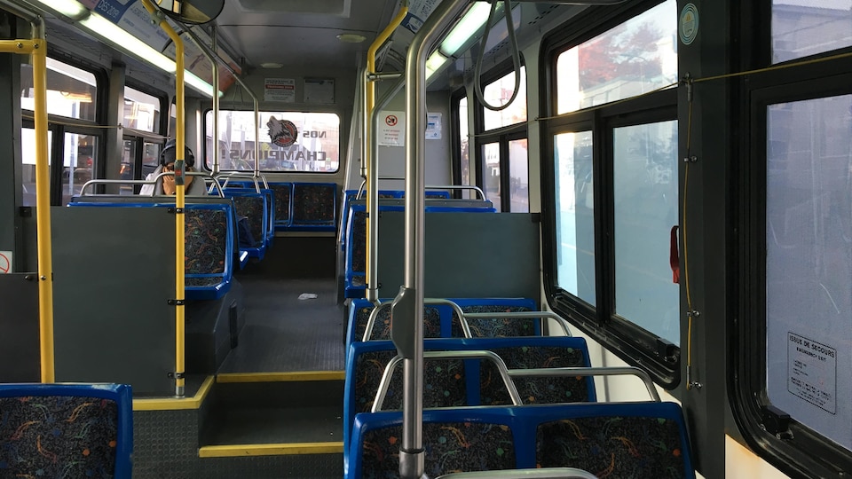 Une personne est assise dans un autobus de ville. Les autres bancs sont vides.