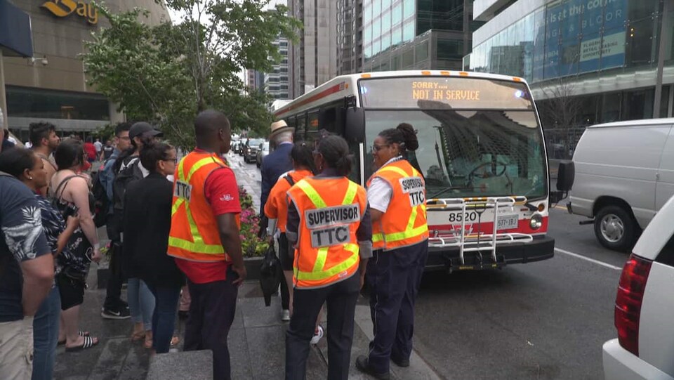 Photo de superviseurs portant un dossard orange et d'usagers qui attendent de monter à bord d'un autobus.