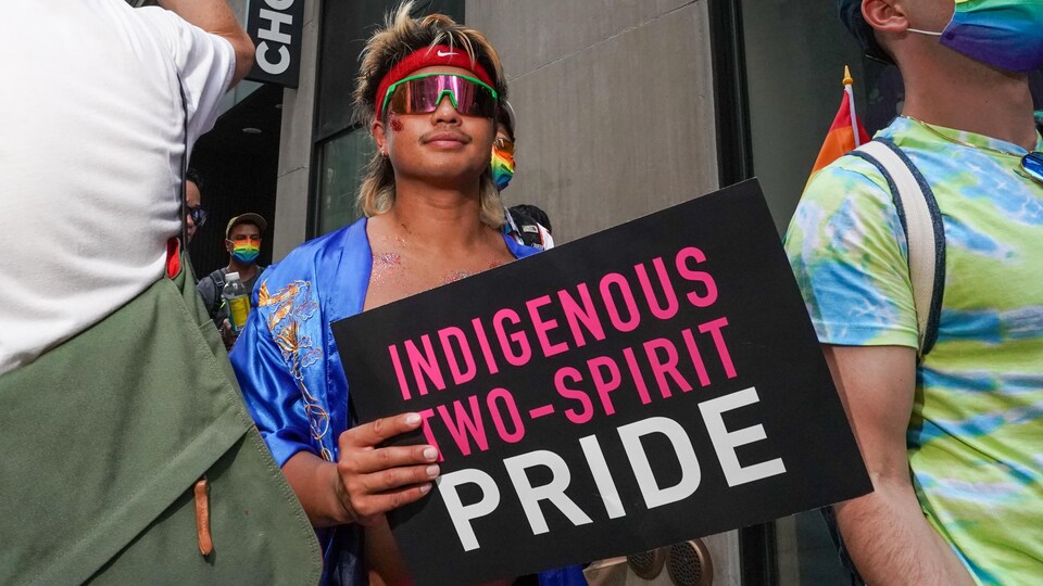 Une personne marche dans la rue avec un panneau indiquant "fierté, bispiritualité autochtone".