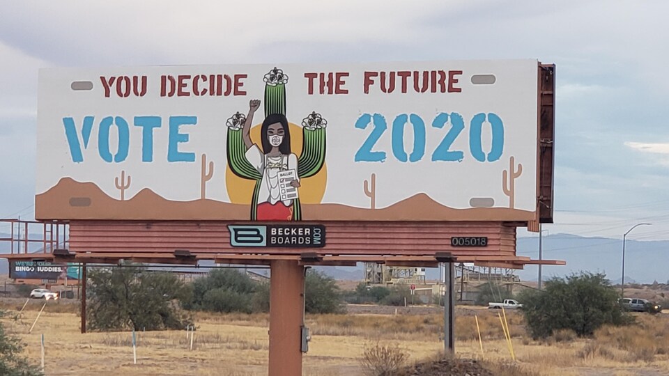 Une pancarte dans une communauté autochtone représente une femme autochtone portant un bulletin de vote pour les élections de 2020 et l'inscription ''vous décidez du futur''.