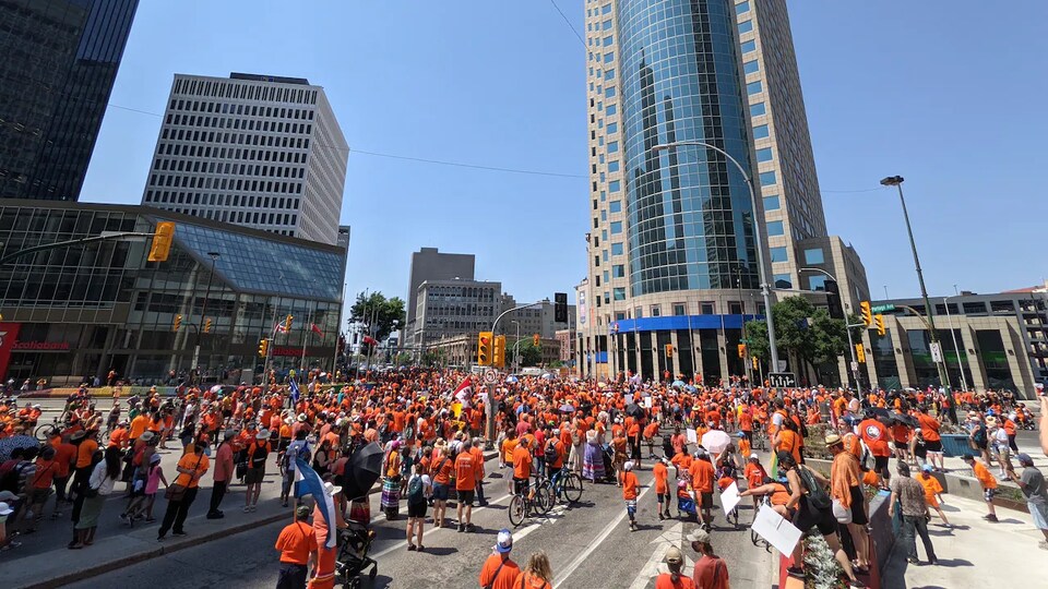 Les rues inondées de personnes qui défilent habillées d'orange. Elles circulent dans le centre-ville de Winnipeg, par une journée ensoleillée. 