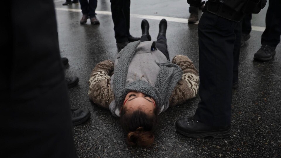 Une manifestante autochtone est allongée au sol, entourée de policiers dont on ne voit que les bottes.