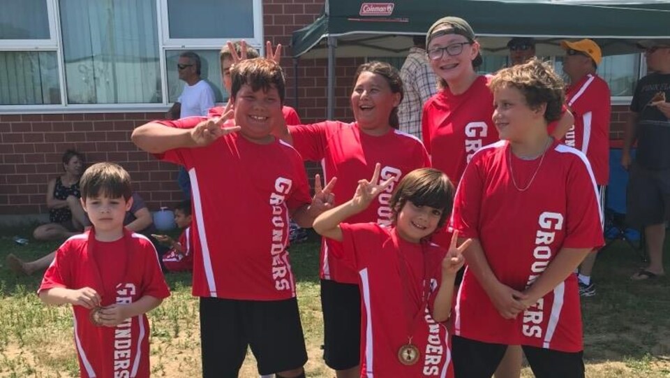 Des enfants de la Première Nation d'Eel Ground vêtus de rouge montrent leurs médailles après leur match de soccer.