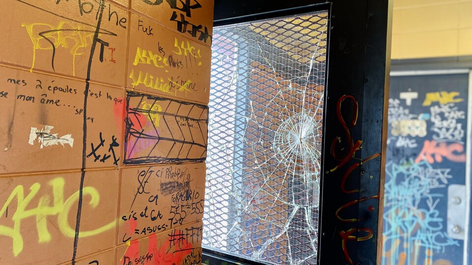 Un mur orange rempli de graffitis et une porte vitrée dont la vitre est cassée.