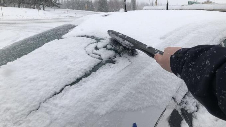Un gendarme passe un balai à neige sur le pare-brise de sa voiture.