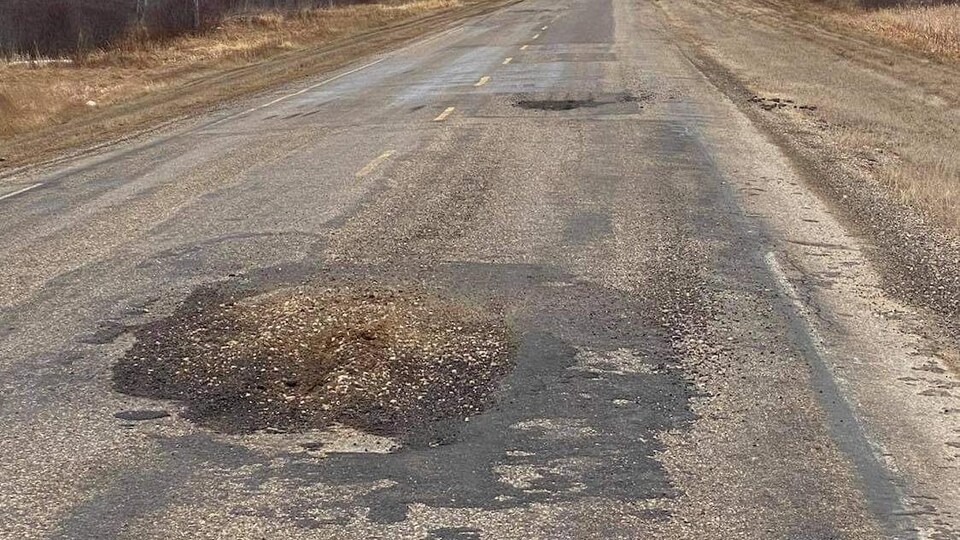 Une route, bordée de rangées d'arbres, et dans laquelle il y a plusieurs trous.