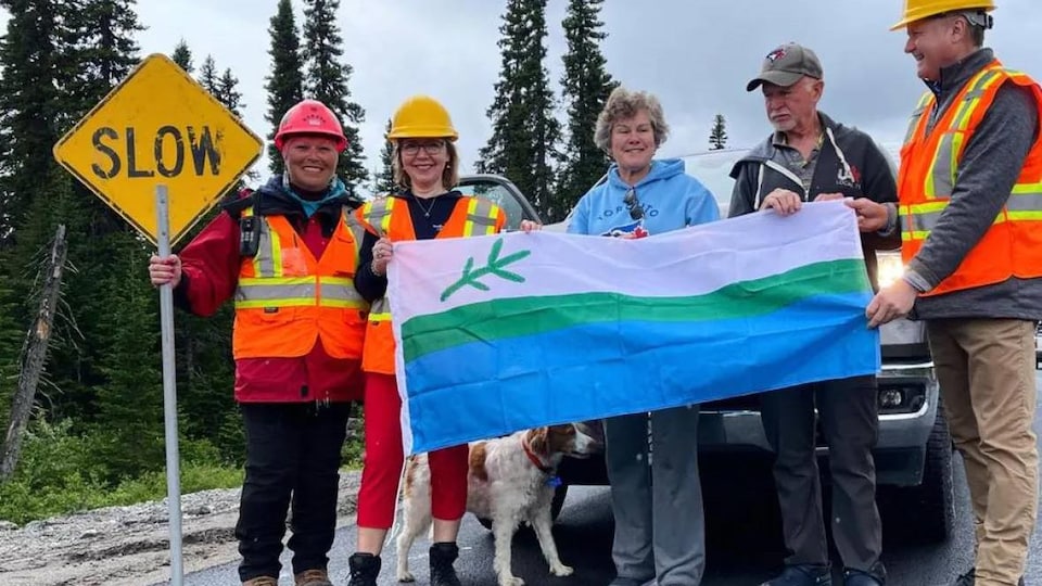 Des travailleurs et deux ministres sont debout sur la route et sourient en exhibant un drapeau du Labrador.