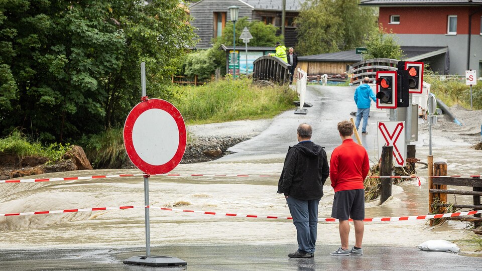 Des personnes observent l’eau qui recouvre une voie ferrée.