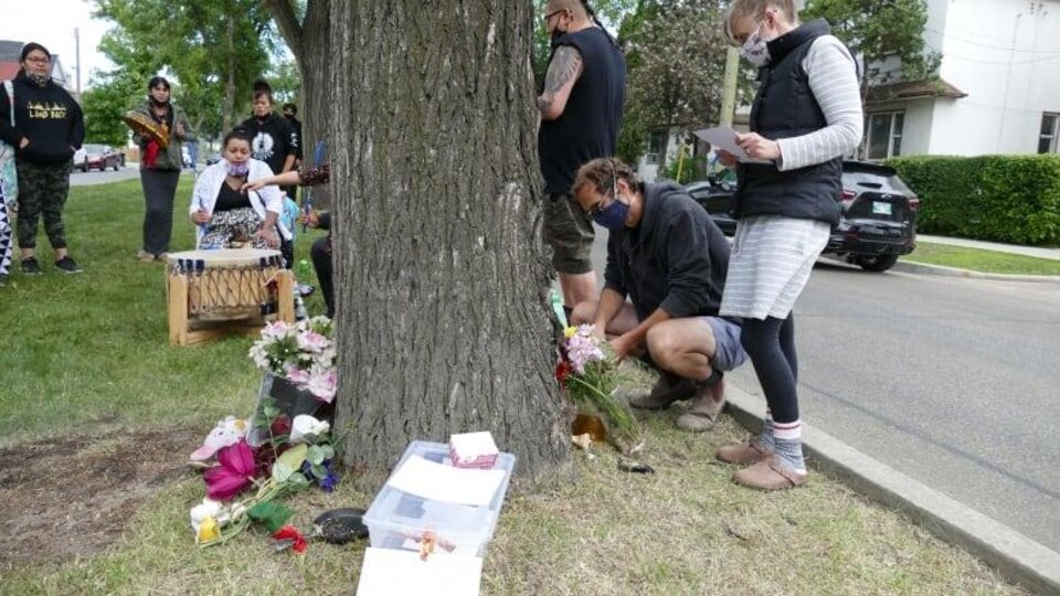 Des gens déposent des fleurs près d'un arbre.