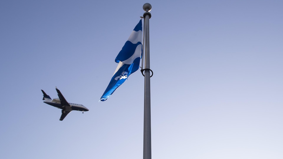 Un petit avion s'apprête à atterrir. Un drapeau du Québec se trouve à l'avant-plan de l'image.