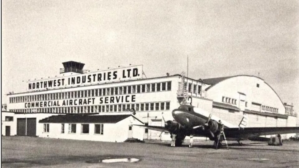 Photo d'époque du hangar 11 où il est inscrit Northwest Industries LTD, commercial aircraft service. Un avion est tout près du bâtiment.