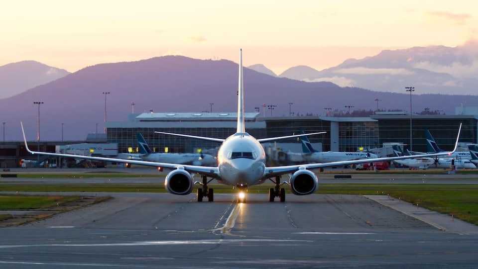 Un avion sur la piste. Des montagnes pourpres et un lever de soleil derrière.