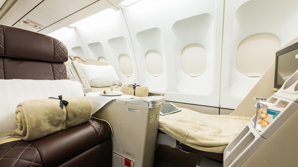 Deux sièges de l'avion privé de luxe 9H-BIG, dont l'un est déployé en couchette, face à un écran de télévision fixé au siège qui se trouve devant.