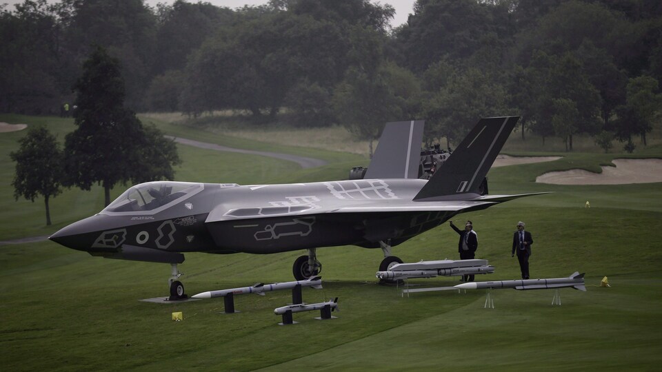 Un avion de chasse de type F-35 exposé au milieu d'un terrain vide, sur de la pelouse, entouré d'arbres.