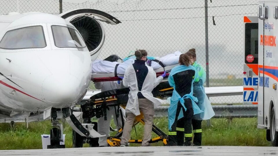 Quatre infirmiers sortent un patient en civière d'un avion.